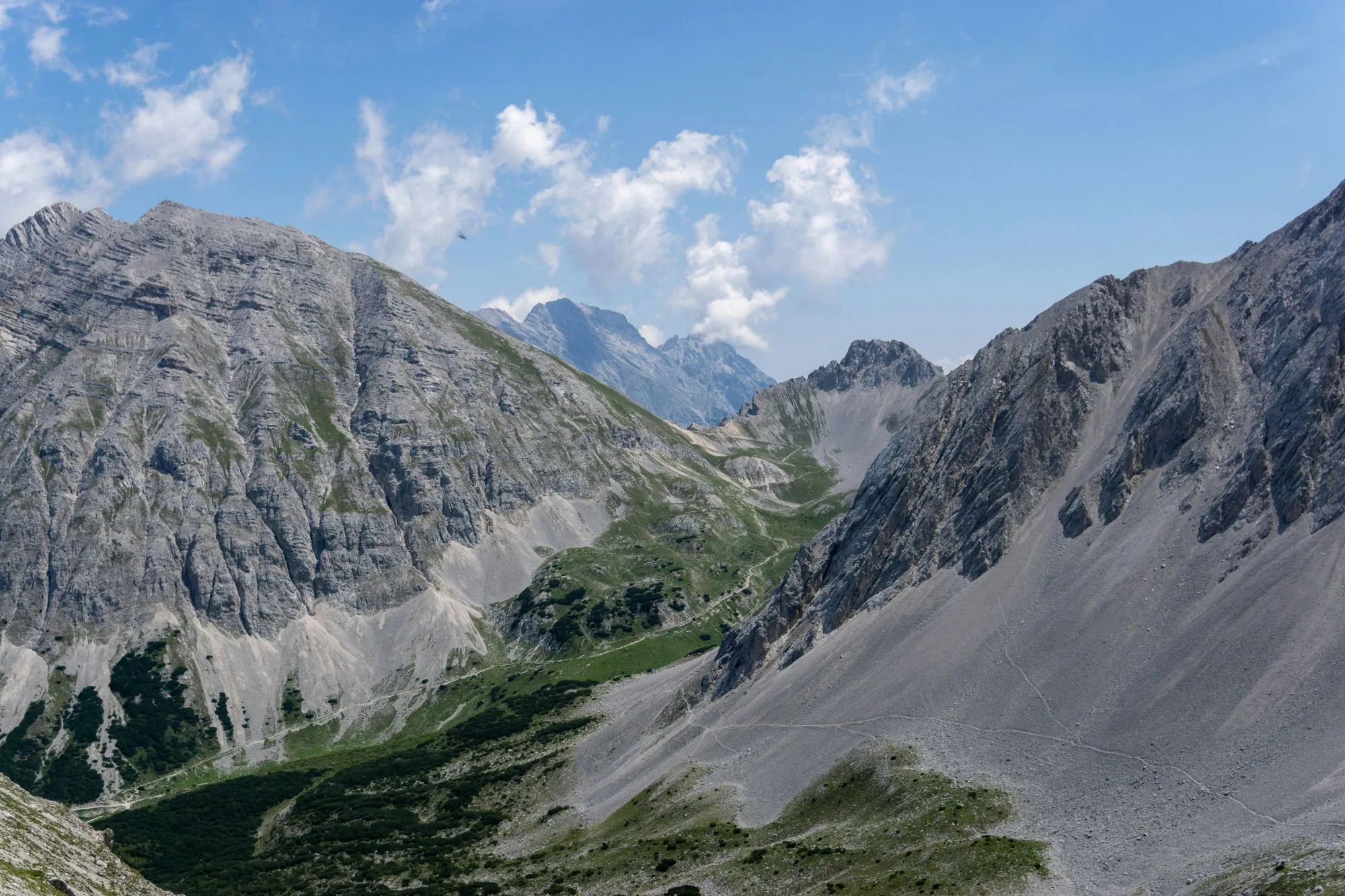 A limestone valley between grey peaks, a trail winding up through green pine scrub